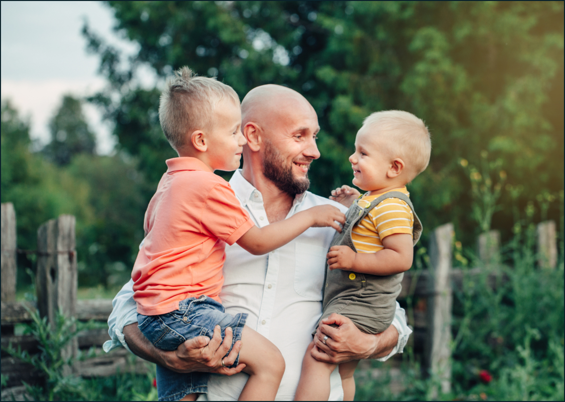 Smiling Man Holds Two Young Children In Arms