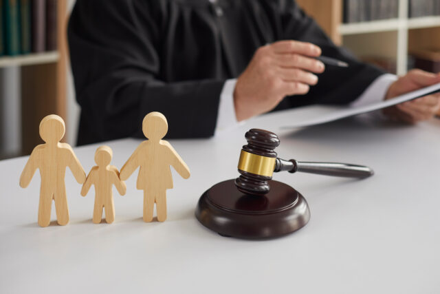 Close up of wooden figurines of family with child and gavel on background of judge conducting divorce process. Concept of alimony, family law and child custody.